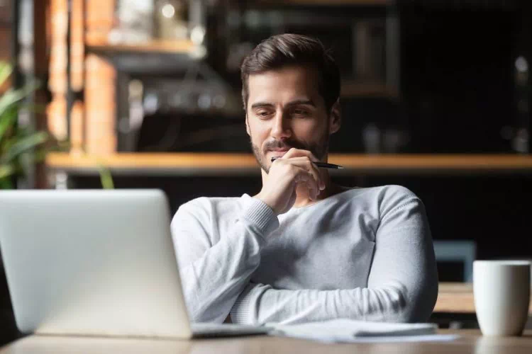 Jeune homme chez lui travaillant sur son ordinateur avec une tasse de café