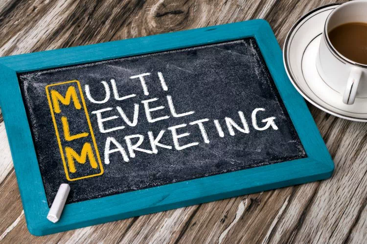 Table sur laquelle se trouve une tasse de café et une ardoise sur laquelle est écrit : Multi Level Marketing