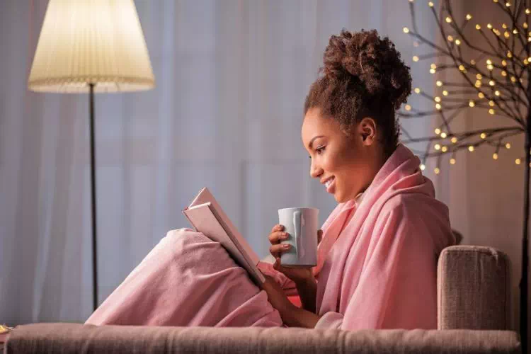 Femme chez elle confortablement assise dans son canapé en train de lire et boire un café