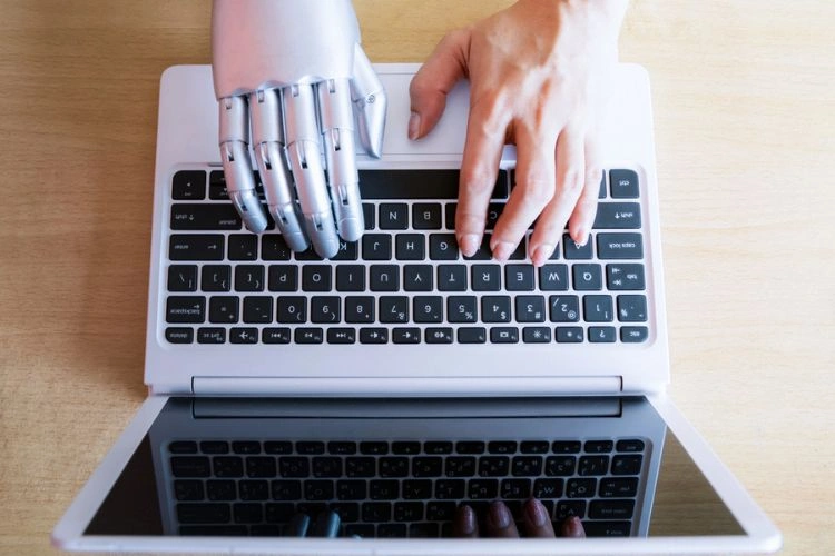 Main de robot et une main humaine appuyant sur un clavier pour représenter l'ingénieur en Intelligence Artificielle