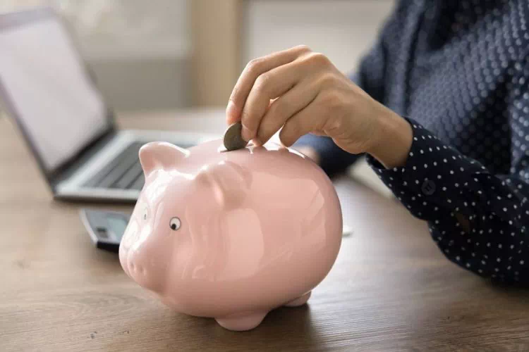 Concept de cagnotte en ligne : personne mettant de l'argent dans une tirelire avec son ordinateur à côté