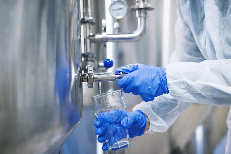 Vue rapprochée des mains dans des gants de protection, ouverture de a vanne du robinet et remplissage du verre avec des-echantillons du reservoir de la machine industrielle